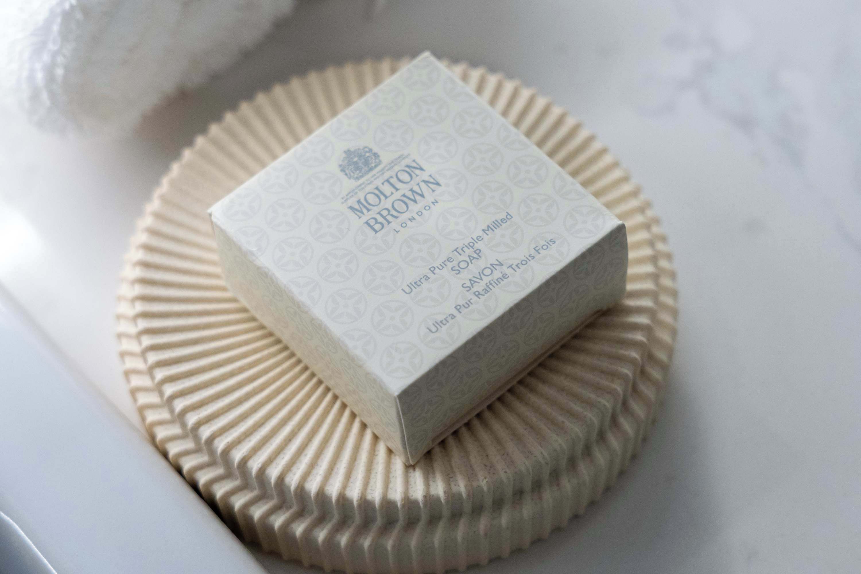Una confezione di sapone Molton Brown su una superficie bianca e strutturata.