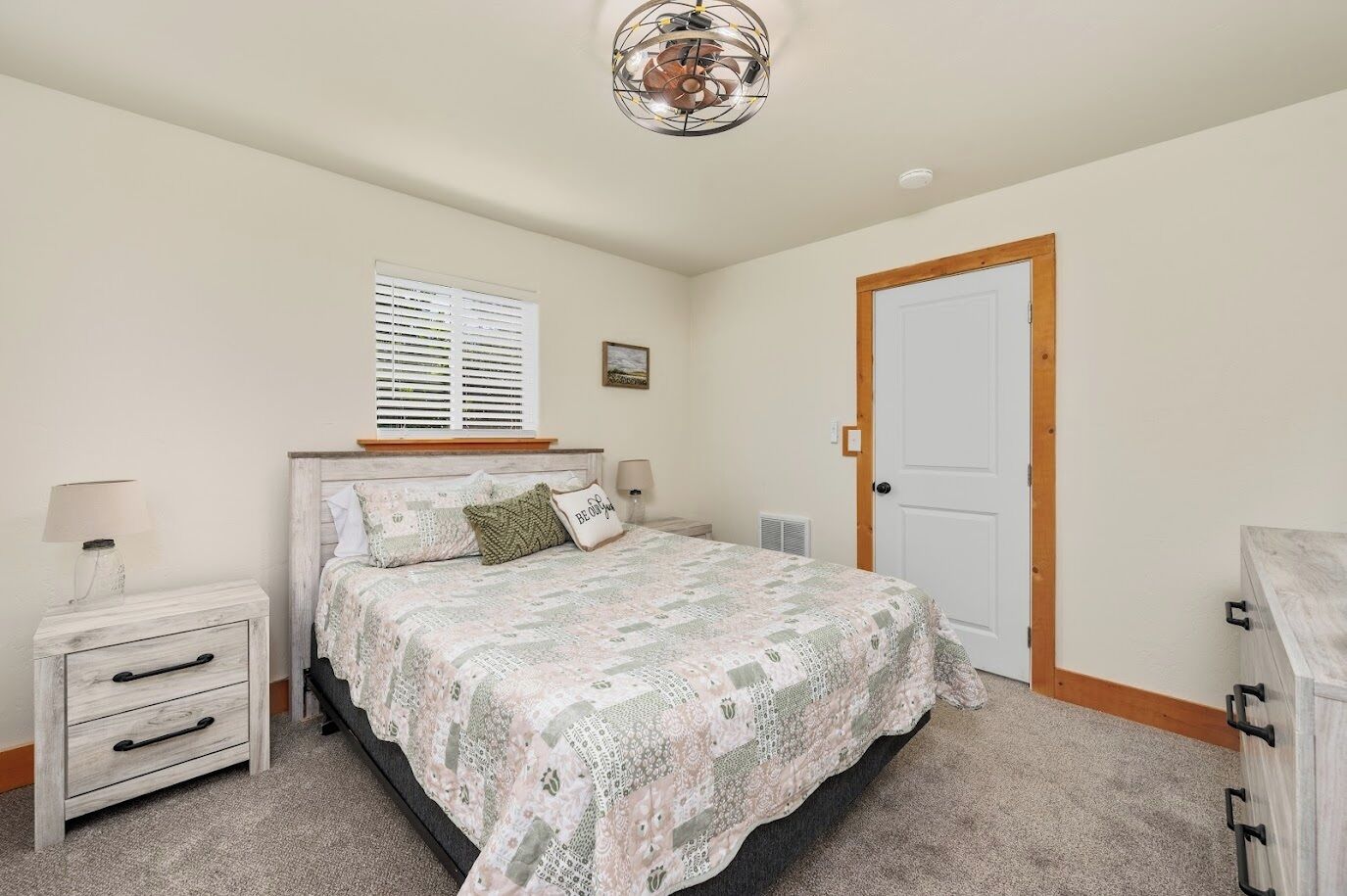 A bedroom with a bed, bedside tables, a lamp, a window with blinds, a door, and a ceiling fan.
