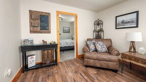 A cozy living room with a brown leather sofa, a wooden console table, and a mirror. A framed picture and a small table lamp are on the wall.