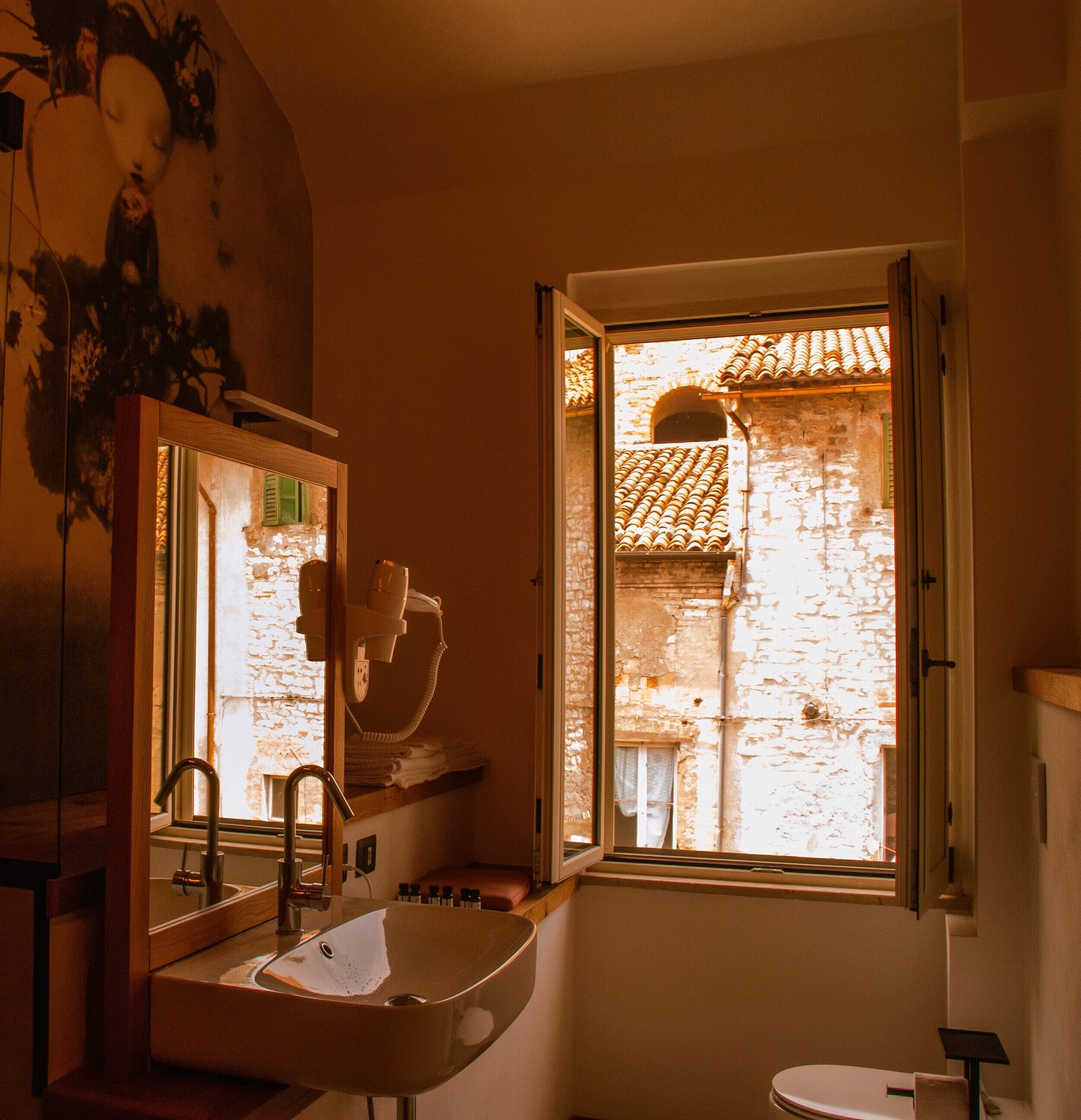 Un baño con lavamanos, espejo y ventana abierta.