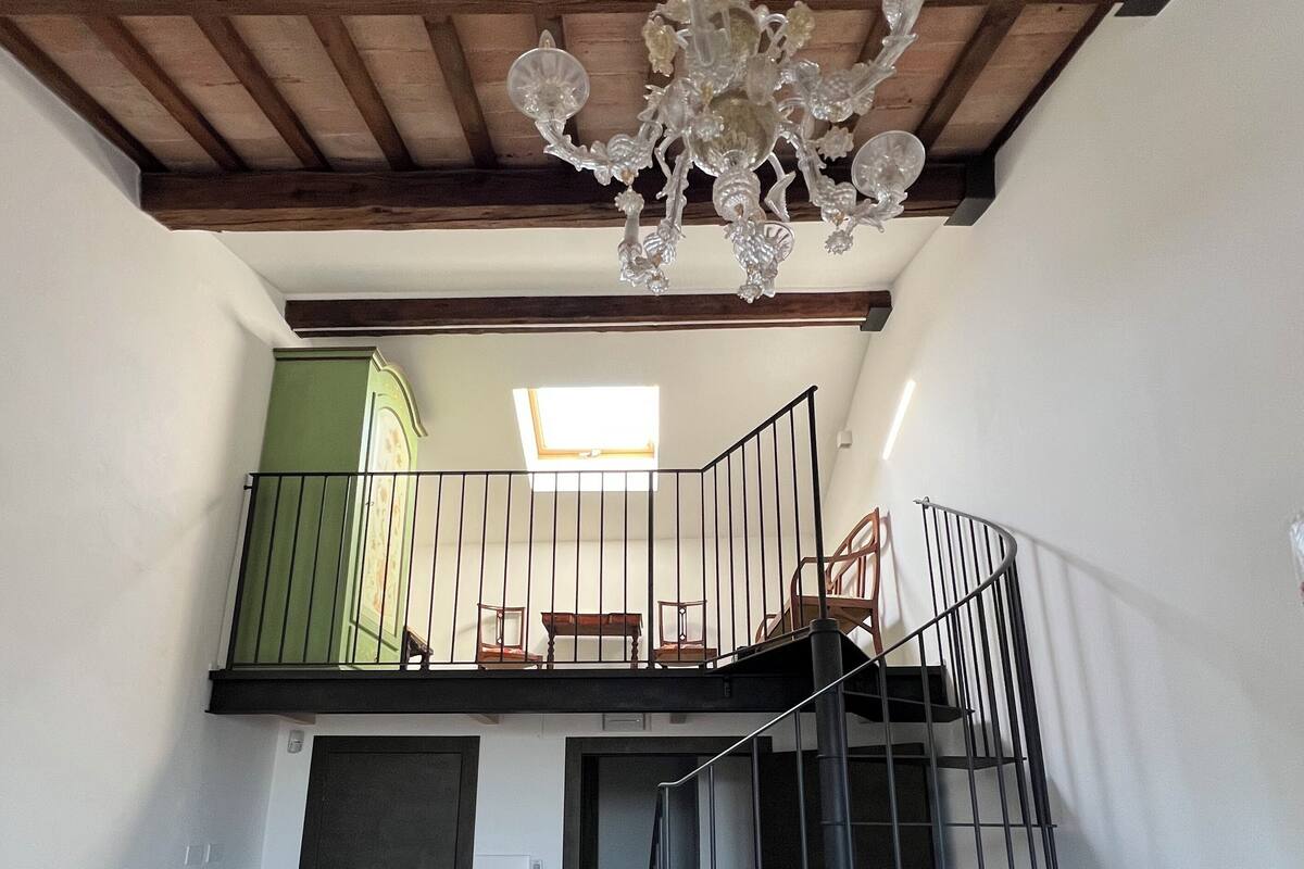 Ein Zimmer mit Holzboden, einer Treppe, einem Balkon mit Geländer und einer Chandelier.