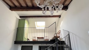 A room with a wooden floor, a staircase, a balcony with a railing, and a chandelier.
