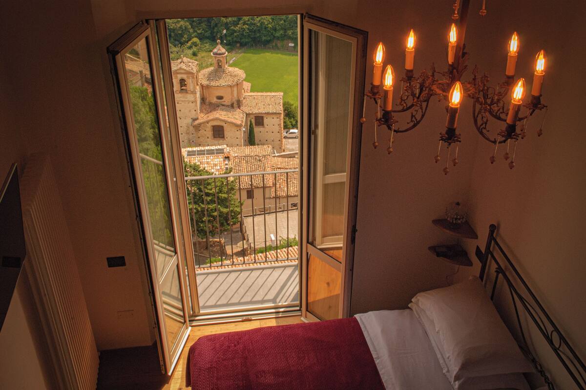Ein Schlafzimmer mit Bett, einer Chandelieber und einem Balkon mit Blick auf ein Gebäude.