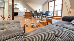 Een moderne loft woonkamer met een glazen salontafel, grijze banken en een eethoek met een groot raam.