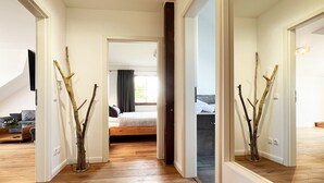 Een gang die leidt naar een slaapkamer met een bed, een houten vloer en een spiegel die de kamer weerkaatst.