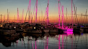 Een jachthaven in de schemering met meerdere zeilboten die aanmeren, verlicht door roze lampen.