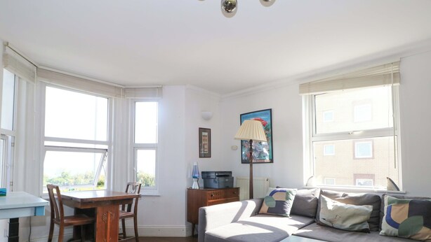 A well-lit living room with a sofa, a small table, a lamp, and a radiator. - Fairhazel Apartment (Hastings)