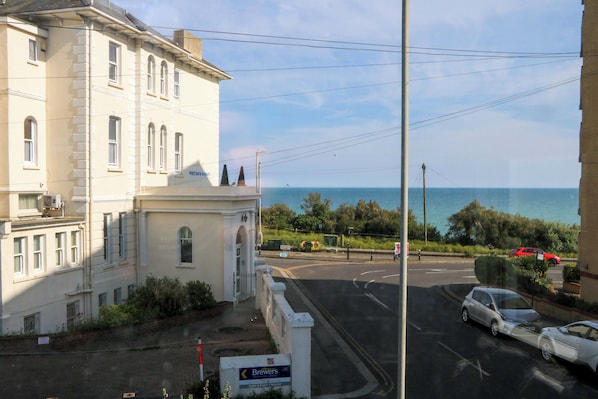 A building with a sign for 'Brewers' on the ground floor, a road with cars, and a view of the sea in the background. - Fairhazel Apartment (Hastings)