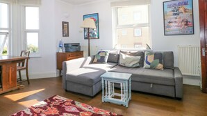 A living room with a grey sofa, a small table, a lamp, and a poster on the wall. - Fairhazel Apartment (Hastings)