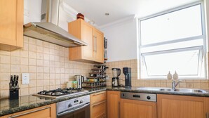 A kitchen with wooden cabinets, a gas stove, an oven, a coffee maker, and a window with a view. - Fairhazel Apartment (Hastings)