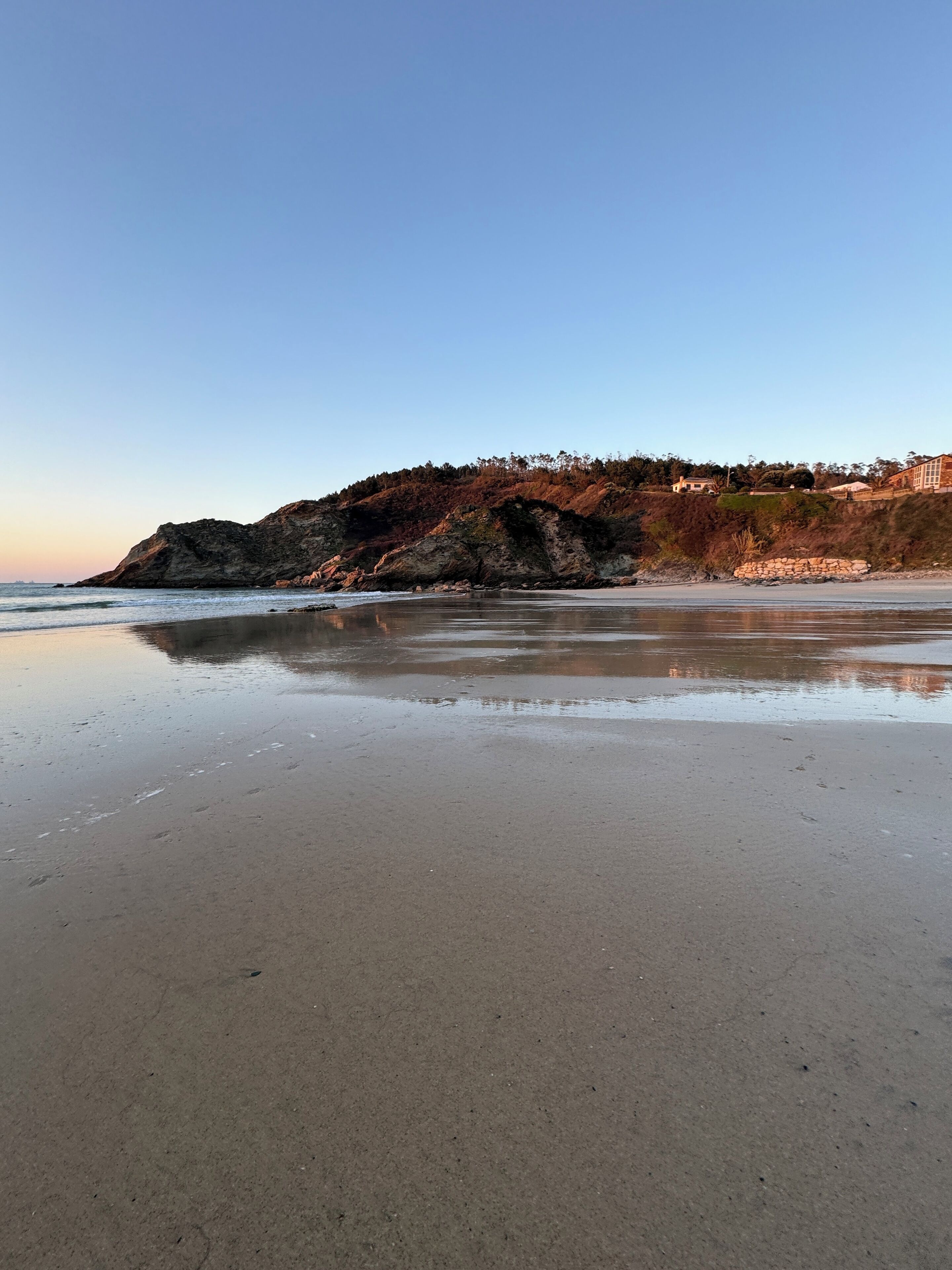 A beach with a rocky cliff and a building in the background.