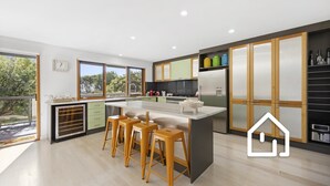 A modern kitchen with a central island, bar stools, a refrigerator, and a view of the outdoors. - Lookout & Sea *1 NIGHT FREE* Beachfront Bliss in McCrae (McCrae)