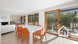 A modern kitchen with white cabinets, a dining area with a white table and orange chairs, and a large sliding glass door leading to a balcony with a view of trees. - Lookout & Sea *1 NIGHT FREE* Beachfront Bliss in McCrae (McCrae)