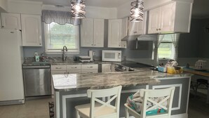 Una cocina moderna con armarios blancos, encimera de mármol, refrigerador de acero inoxidable y microondas integrado.