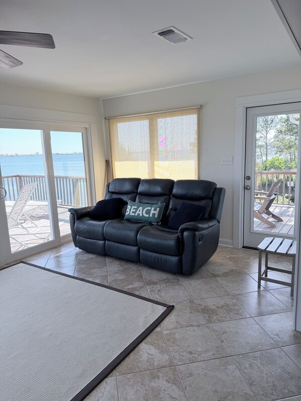A room with a black leather sofa, a view of the sea, and a patio area with a wooden deck.