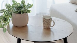 Una mesa redonda de madera con una taza blanca y una planta en maceta.