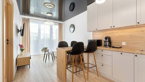 Cocina moderna con armarios de madera, comedor con mesa de madera y sillas negras, y un ventanal que proporciona luz natural.