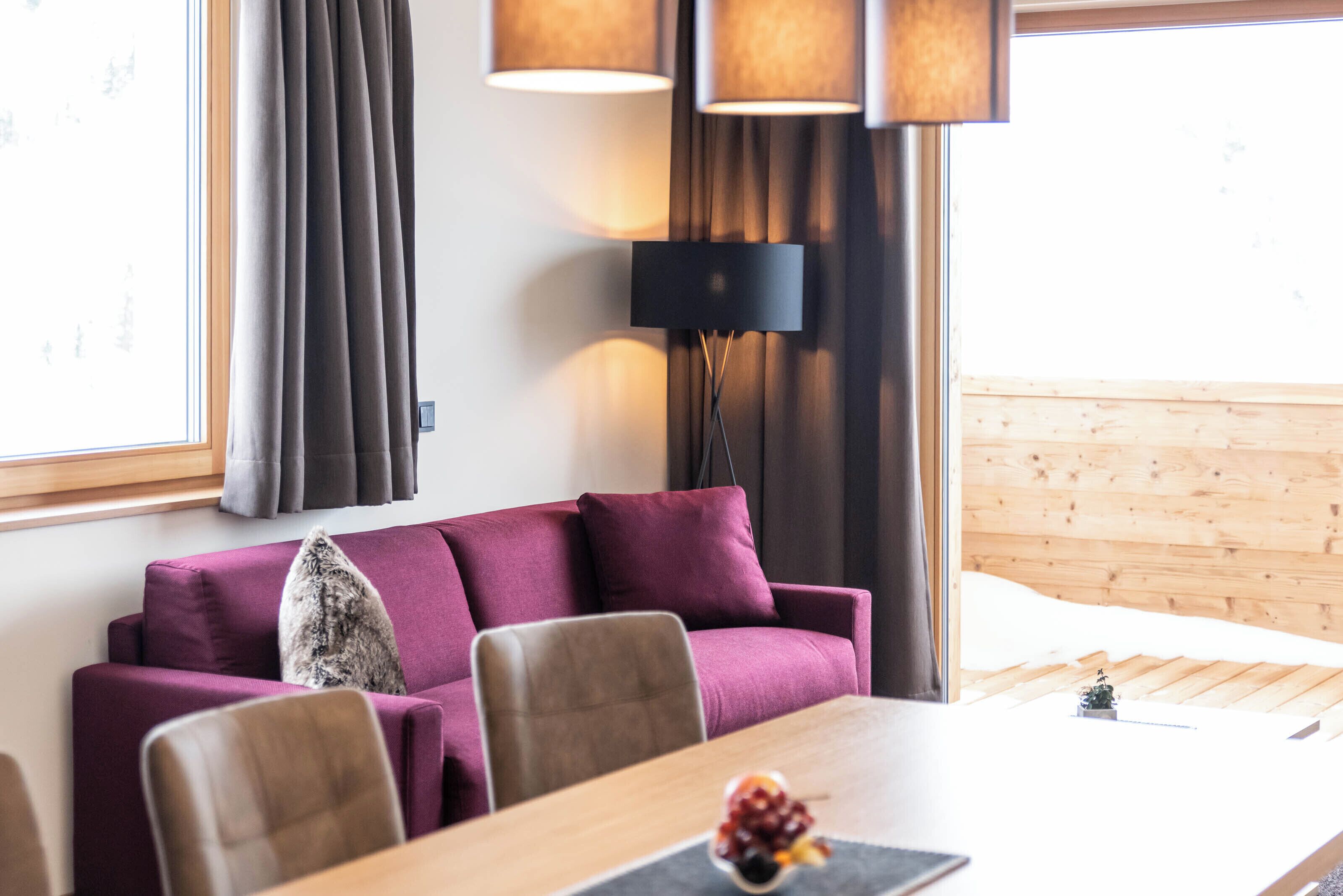 Una sala de estar moderna con un sofá púrpura, una mesa de comedor de madera y una lámpara de pie negra.