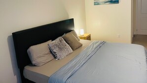 Een netjes opgemaakt bed met een zwart hoofdeinde, een bedlampje en een schilderij aan de muur.