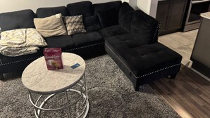 Een woonkamer met een zwarte modulaire bank, een ronde salontafel en een keuken op de achtergrond.