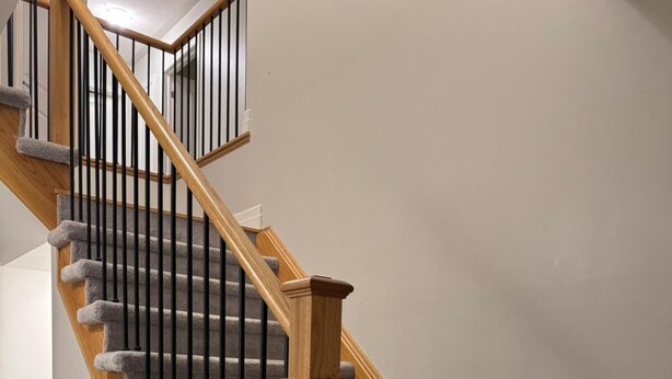 Een trap met houten leuningen en zwarte spijbels, bekleed met tapijt, en een effen muur.