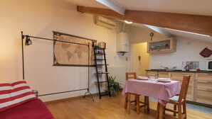 Ein gemütliches Zimmer mit Holzboden, einem rot-weißen karierten Tisch, einem Holzstuhl, einer roten Couch, einer Weltkarte an der Wand, einer Leiter und einer Küchenzeile mit Mikrowelle und Wasserkocher.