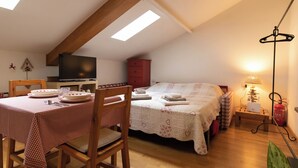 Ein gemütliches Zimmer mit Esstisch für zwei Personen, einem Bett mit floralem Überwurf, einem Fernseher und einer Lampe.