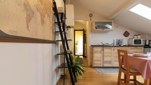 Eine Küche mit Holzschränken, einem Esstisch mit kariertem Tischläufer und einer an der Wand angelehnten Leiter.