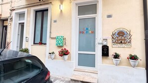A building with a sign reading "MAX FORTUNA" and "GUEST HOUSE" with a logo. There are potted plants on the ground floor and a car parked in front. - MAX-FORTUNA (Ragusa)
