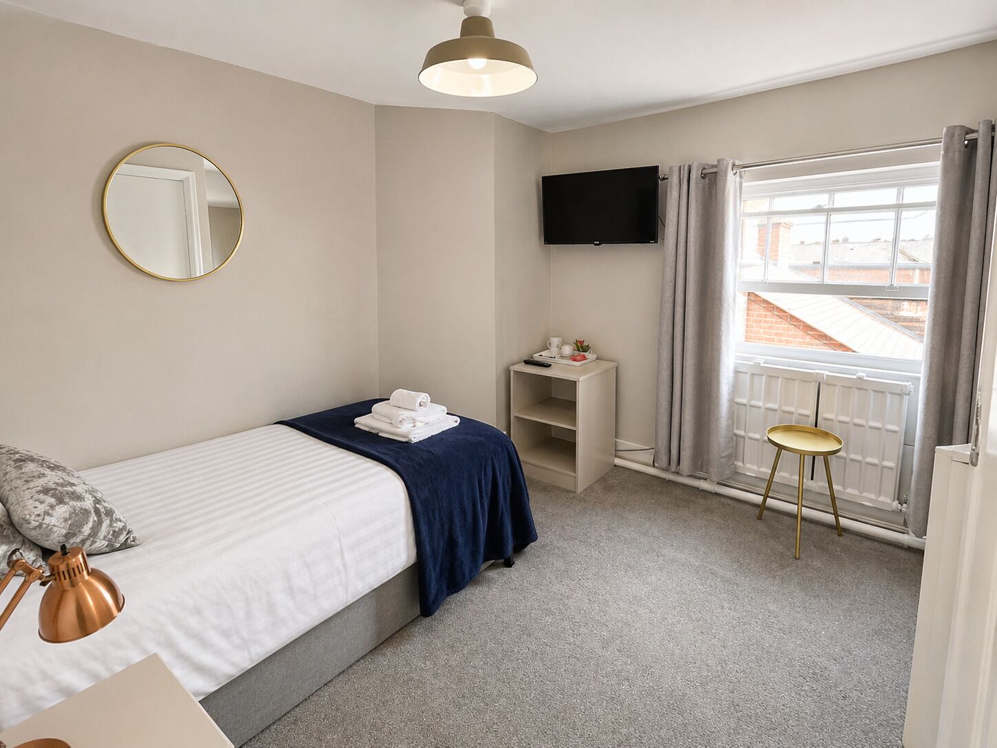 A bedroom with a bed, a bedside table with a TV, a chair, and a window with curtains.