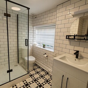 Un baño con cabina de ducha de vidrio, inodoro, lavabo y ventana con persianas.