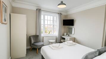 Una habitación de hotel con una cama, una silla, un escritorio con espejo, televisión y ventana con cortinas.