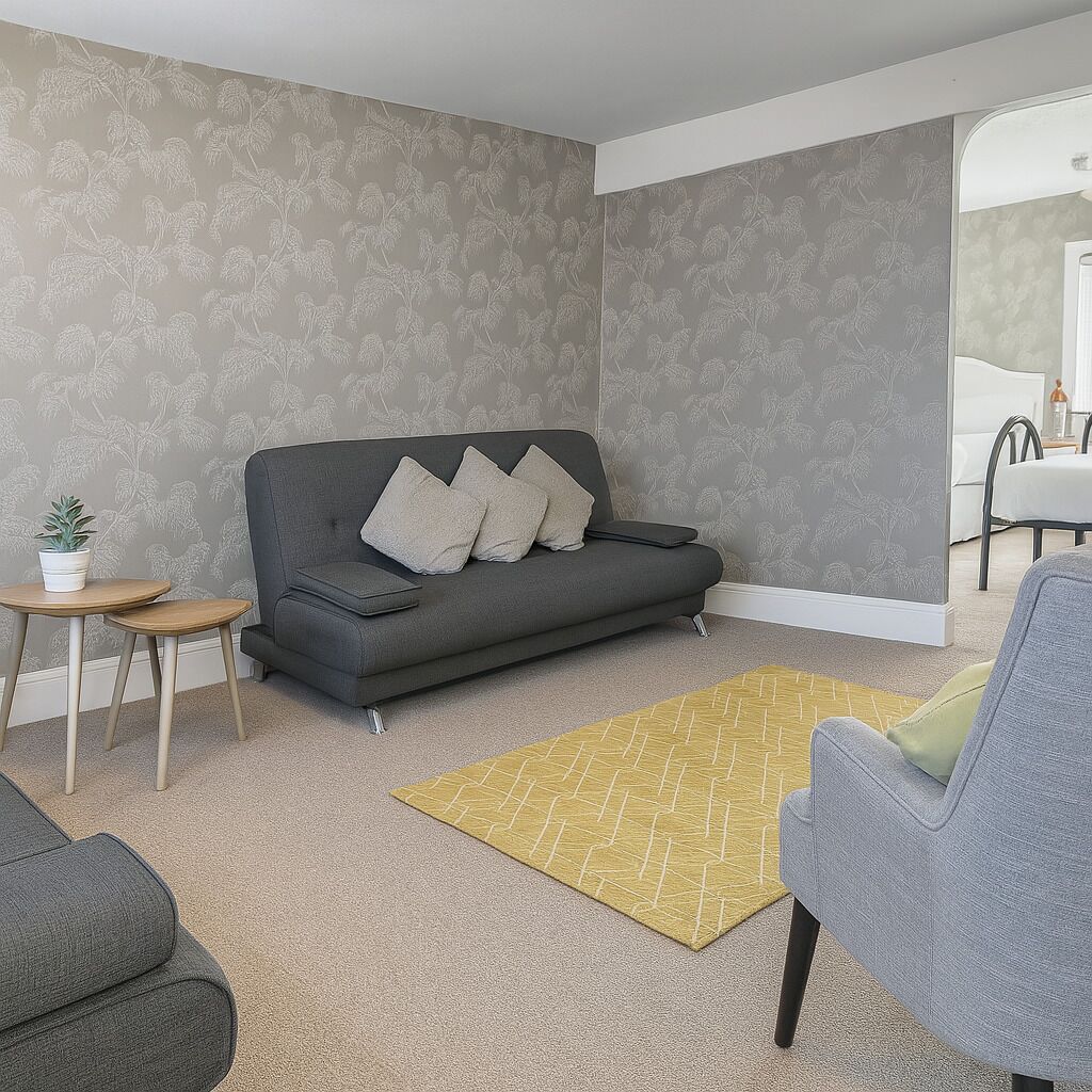 Un salon avec un canapé gris, une petite table d’appoint sur laquelle est posée une plante, un tapis jaune et un fauteuil gris.