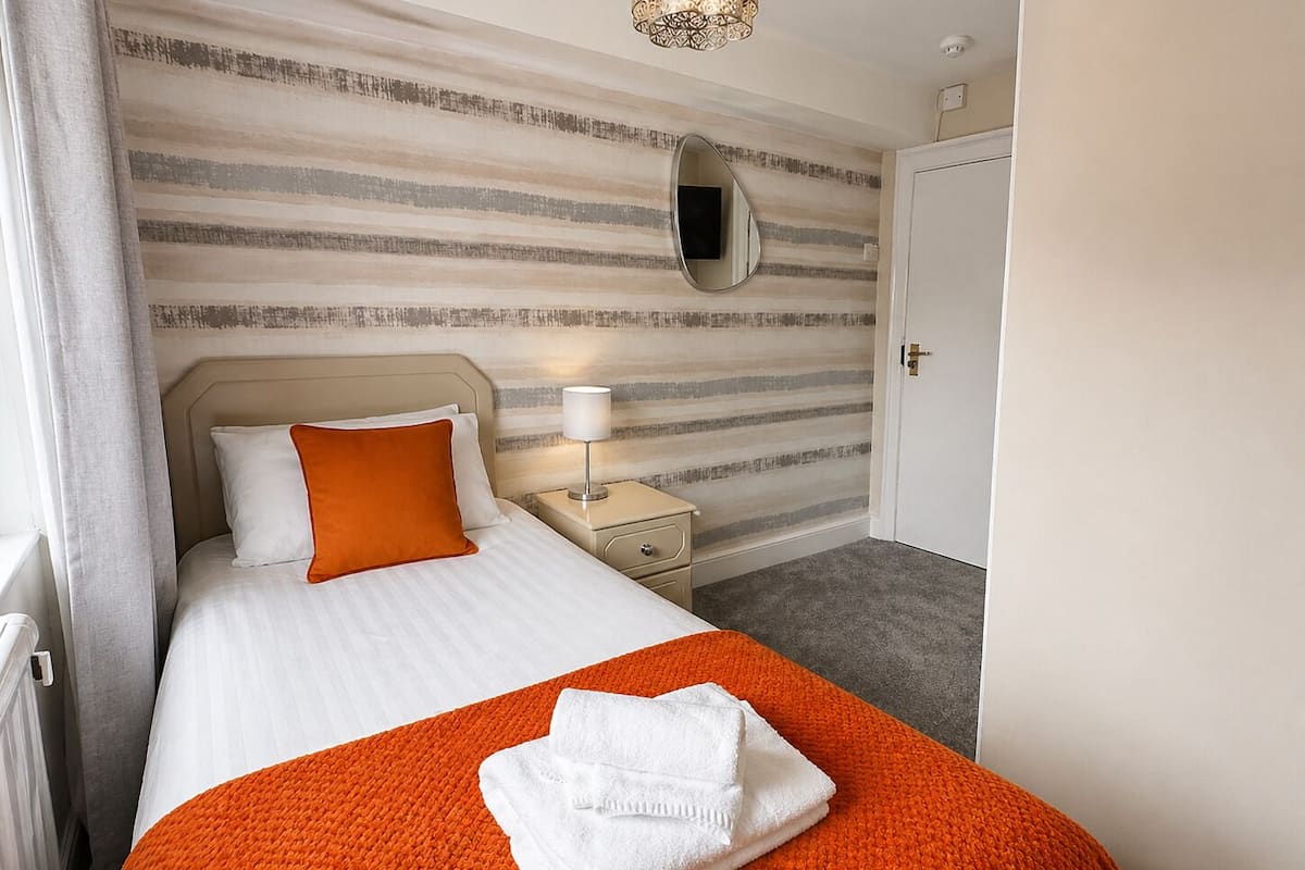 A hotel room with a bed, a nightstand, a lamp, a mirror, and a door.
