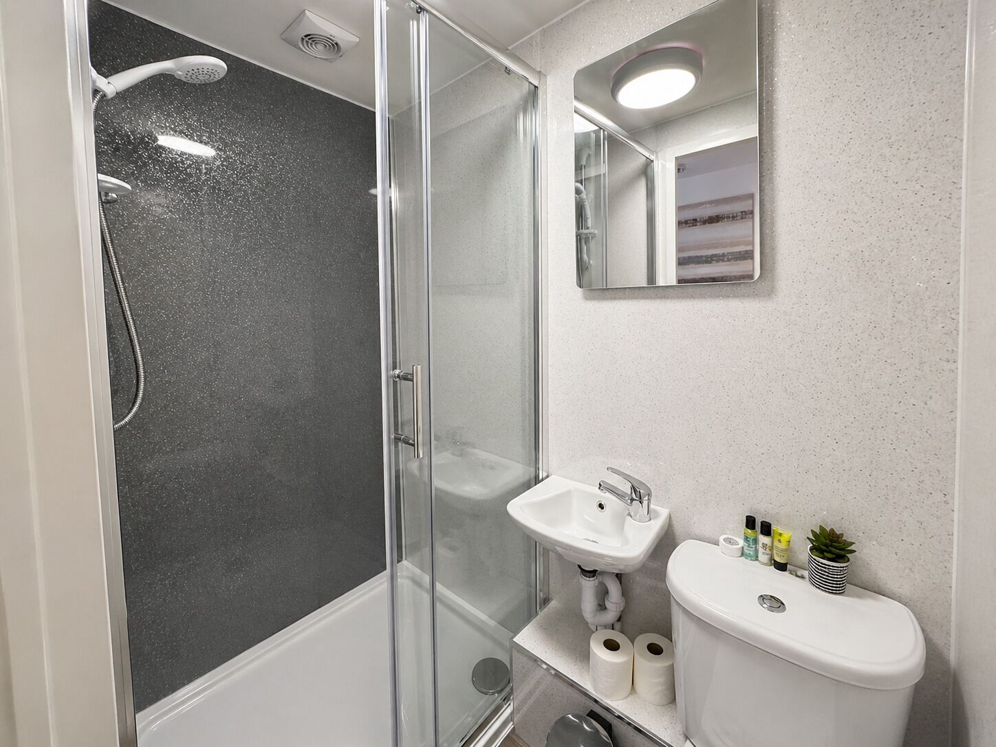Un bany modern amb dutxa tancada amb vidre, un lavabo blanc i un vàter.