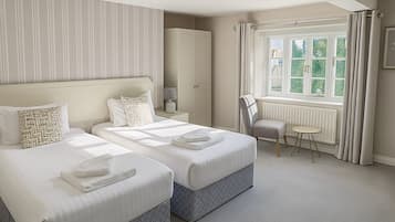 A hotel room with two beds, a desk, a chair, a radiator, and a window with curtains.