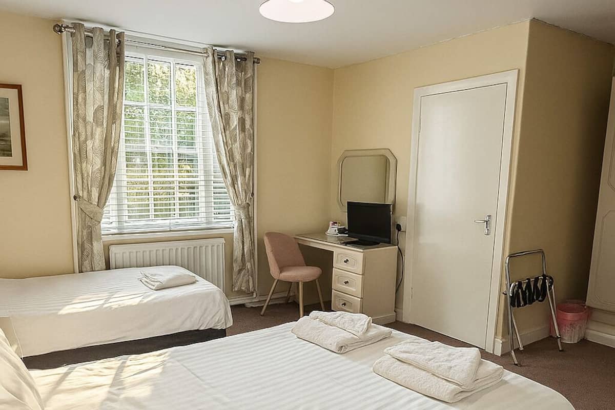 A hotel room with two beds, a desk with a computer, a chair, a radiator, and a door.