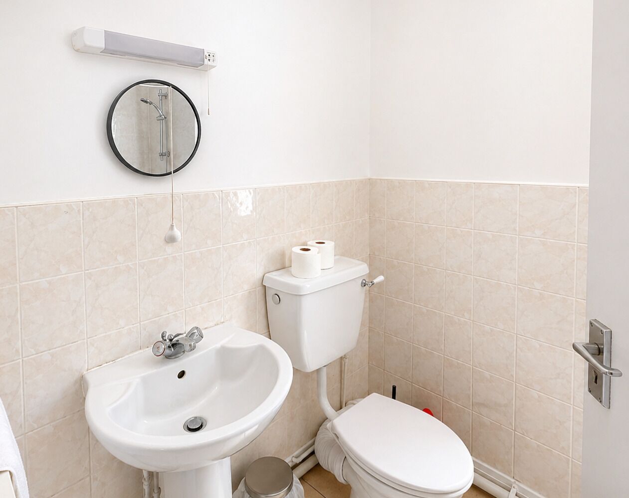 A bathroom with a toilet, sink, and a mirror on the wall.