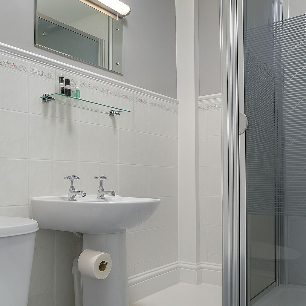 Une salle de bain avec un lavabo blanc, deux robinets, un miroir au-dessus du lavabo et une cabine de douche en verre.