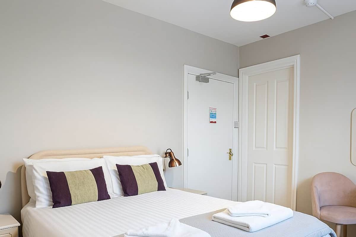 A neatly made bed with pillows, a bedside lamp, and a folded towel on the nightstand.