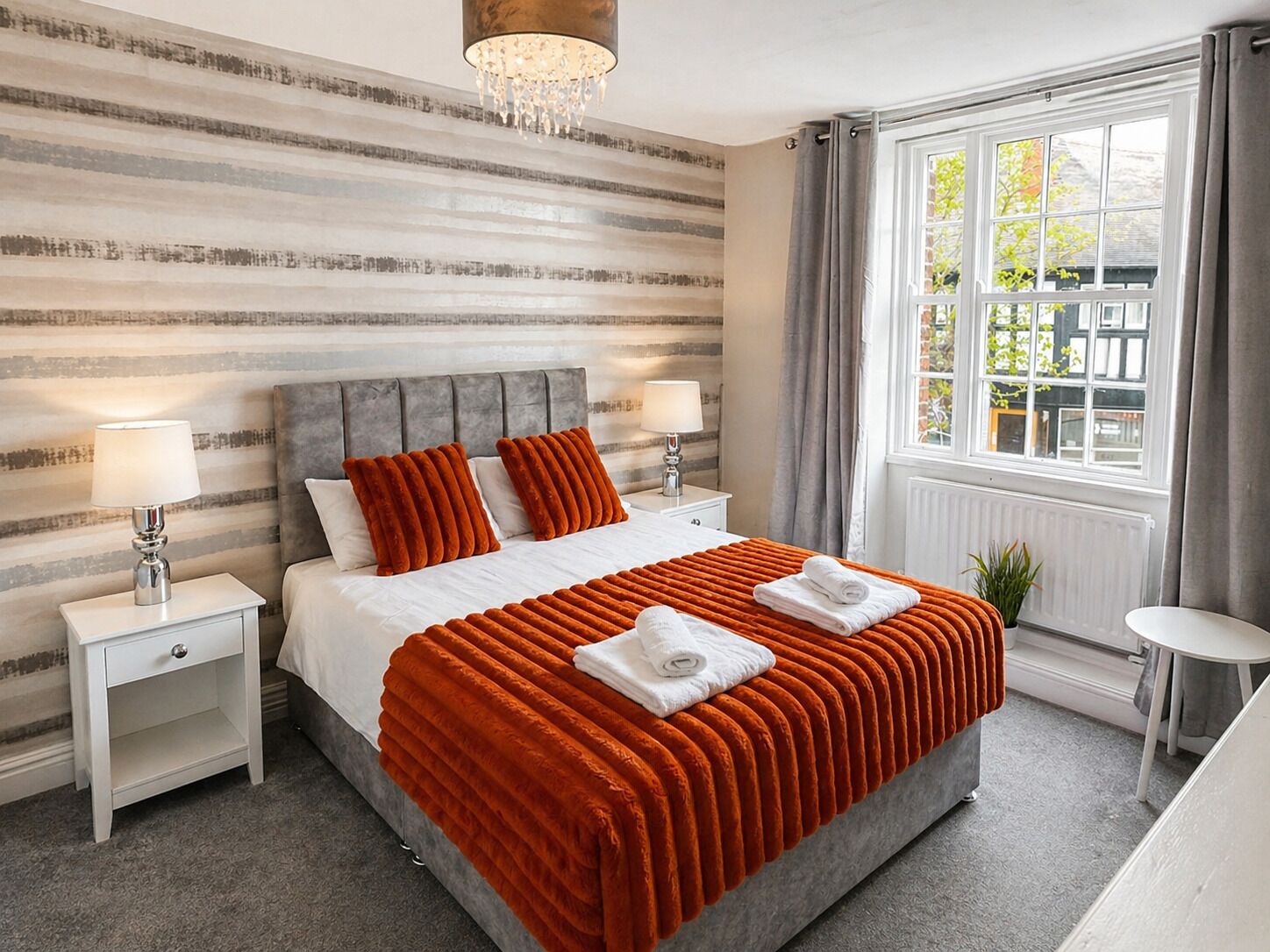 Una habitación de hotel con una cama, dos mesitas de noche, un ventanal con cortinas y un candelabro.