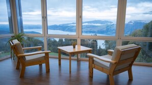A room with a large window offering a view of a lake and mountains. There are two wooden chairs and a small table with a plant on it. - Auszeit-Hotel Z Aeschiried (Retreat Hotel Z Aeschiried) (Aeschi bei Spiez)