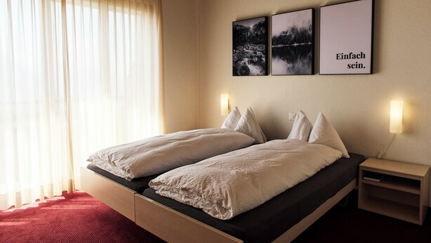 A double bed with white linens, a nightstand with a lamp, and three framed pictures on the wall.