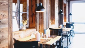 A rustic dining area with wooden walls, large windows, and black pendant lights. Tables are set with white napkins and cutlery. - Auszeit-Hotel Z Aeschiried (Retreat Hotel Z Aeschiried) (Aeschi bei Spiez)