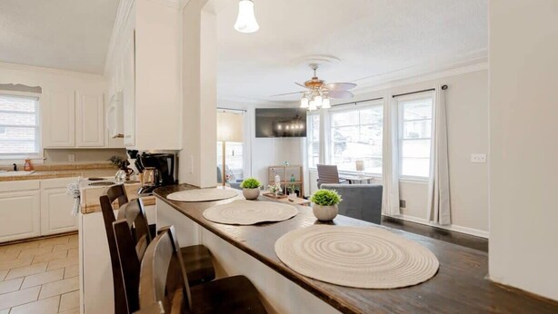 Une cuisine moderne dotée d’un grand îlot central, d’un plan de travail en bois foncé, de meubles blancs et d’un ventilateur de plafond.