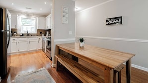 A modern kitchen with white cabinets, a wooden dining table, and a 'welcome' sign on the wall.