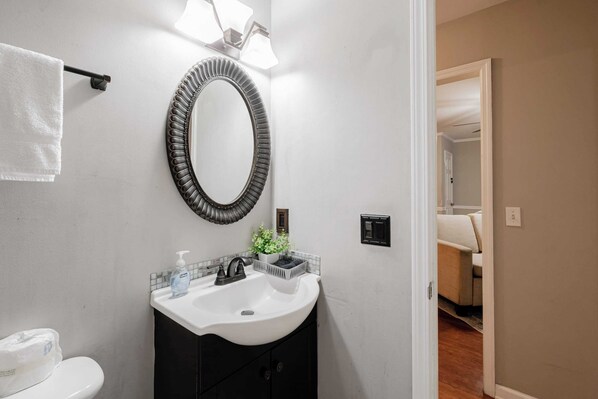 Un baño con un lavabo blanco, armarios oscuros, un espejo redondo y un perchero.