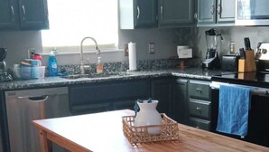 Una cocina con armarios de madera oscura, encimera de granito, mesa de comedor de madera con bancos y una ventana que proporciona luz natural.