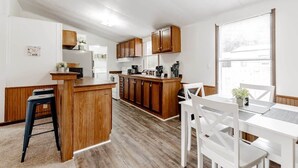 A modern kitchen with wooden cabinets, a central island, and a dining area with white chairs. - 15mins to Downtown- Adorable on Taylor, Both Units (West Columbia)