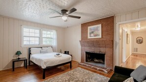 A bedroom with a bed, a fireplace, a ceiling fan, a window, and a door.